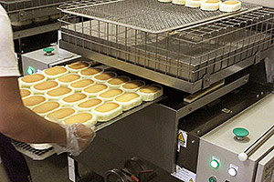 The Grill Marking Machine creates grill marks on the cheese flavor cakes.