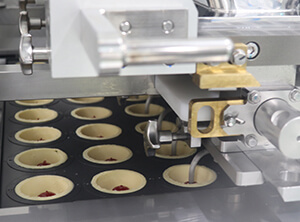 Depositing of tart batter, molding, depositing of jam and more batter is done before going into the oven.