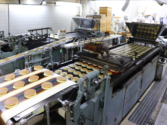 Dorayaki in production. After baking, dorayaki are transported on the conveyor belt in the middle to the workers for them to sandwich the bean paste.
